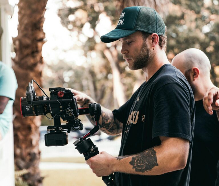 Male videographer working with camera rig during outdoor shoot, showcasing filmmaking process.